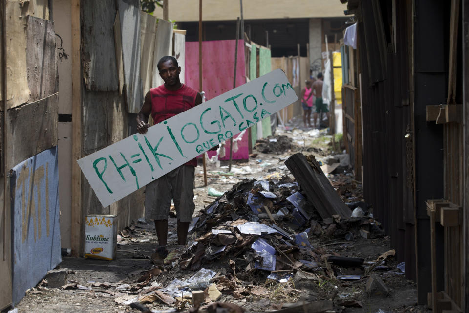 Pedro Pereira holds a sign that reads in Portuguese; "I want a house," and the name of his blog, in an area recently occupied by squatters, in Rio de Janeiro, Brazil, Wednesday, April 9, 2014. Thousands of people have laid claim to a compound of abandoned office buildings owned by the private telecommunications company Oi, and named their settlement after the state-owned telecommunications Telerj. Authorities are negotiating with squatters to leave peacefully from the area they have occupied for more than a week.(AP Photo/Silvia Izquierdo)