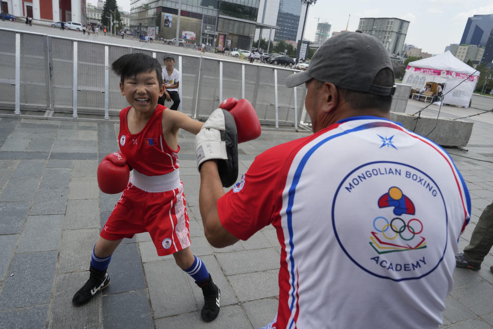 Trainer N.Batbayar helps twelve-year-old Gerelt-Od Kherlen warm up before a bronze medal boxing match on Sukhbaatar Square in Ulaanbaatar, Mongolia, Tuesday, July 2, 2024. Growing up in a Ger district without proper running water, Gerelt-Od fetched water from a nearby kiosk every day for his family. Carrying water and playing ball with his siblings and other children made him strong and resilient. (AP Photo/Ng Han Guan)