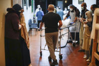 Mourners gather as the body of Mohammad Altaf, who died at 48 of COVID-19, is wheeled into an open space after being ritually washed and wrapped before being given funeral prayers in the Muslim tradition at Al-Rayaan Muslim Funeral Services, Sunday, May 17, 2020, in the Brooklyn borough of New York. (AP Photo/John Minchillo)