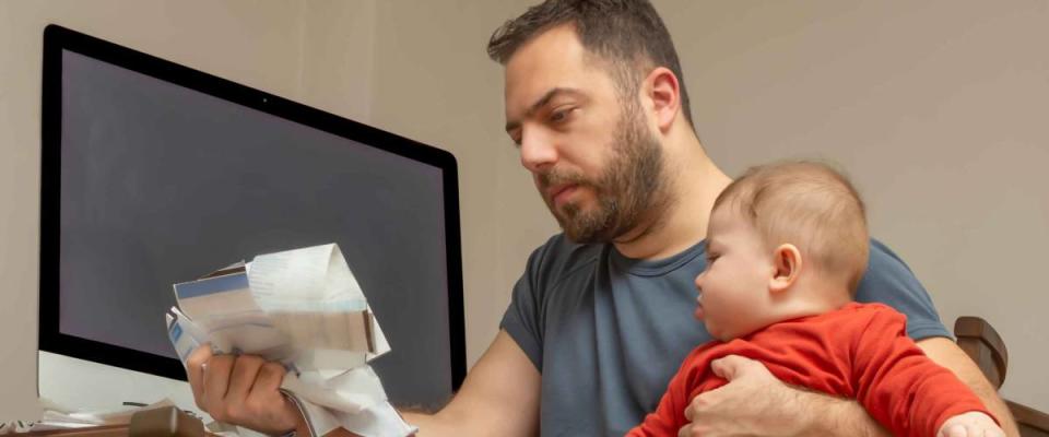 Man holding baby in one arm, looking at bills in other hand