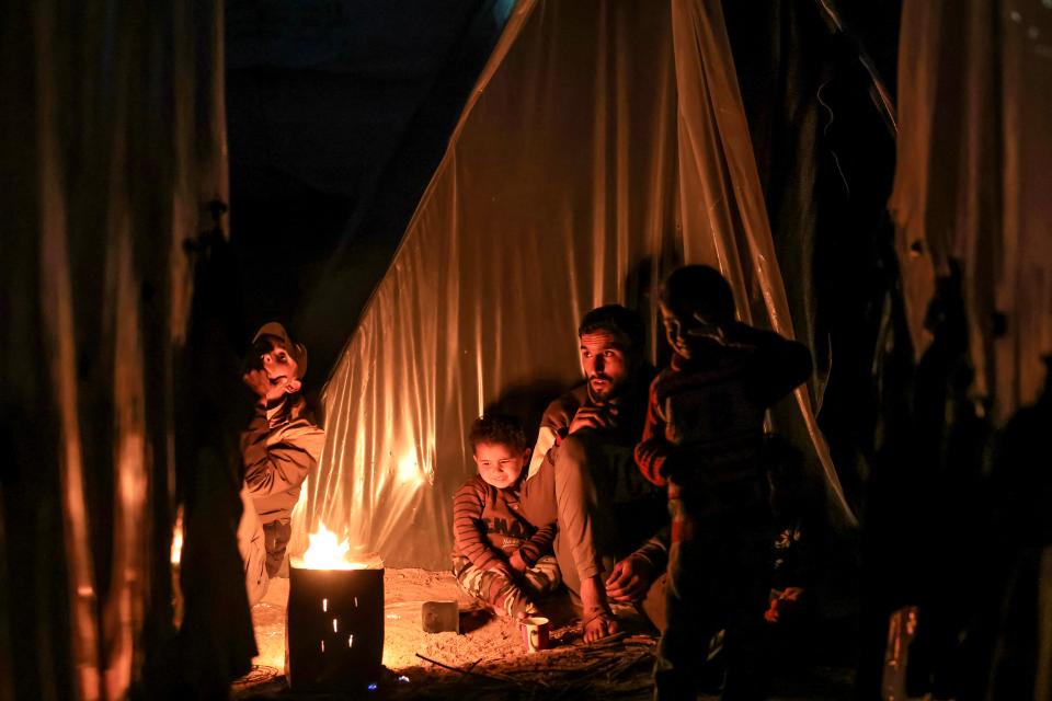 A man sits with children by a fire outside one of the tents housing displaced Palestinians in Rafah in the southern Gaza Strip on Monday.