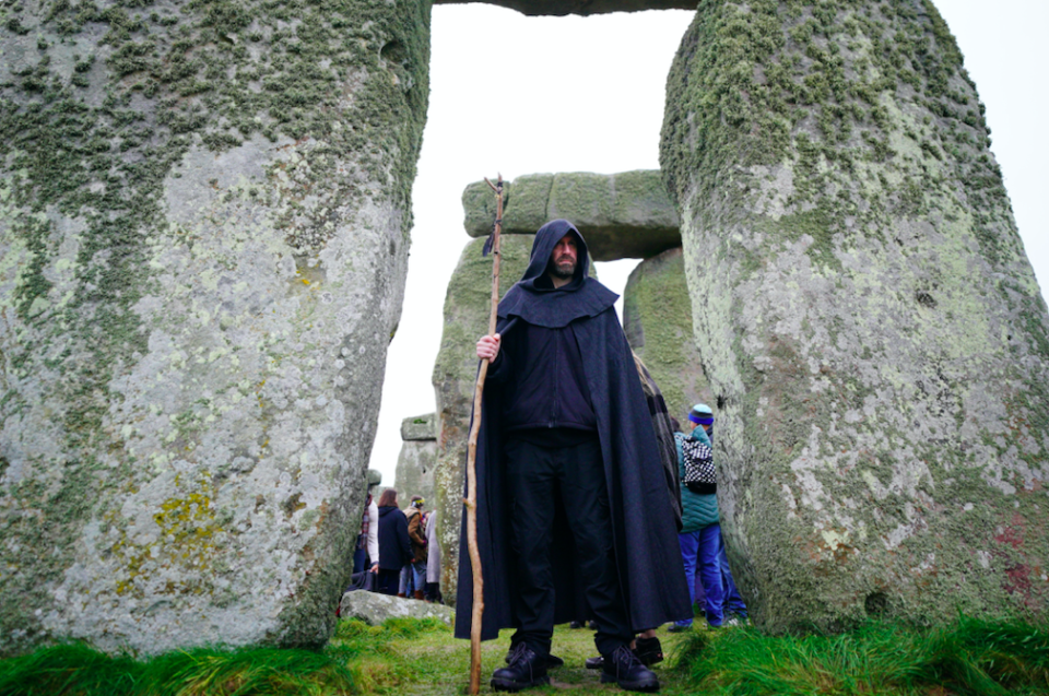 A man wearing robes and carrying a staff stands between two stones as the sun rises at Stonehenge. (PA)