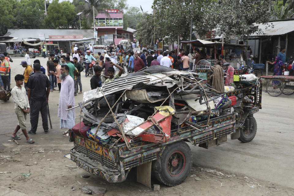 People stand near the wreckage of a bus that fell into a roadside ditch in Shibchar area in Madaripur district, Bangladesh, Sunday, March 19, 2023. More than a dozen people were killed and more were injured in the accident. (AP Photo/Jibon Ahmed)