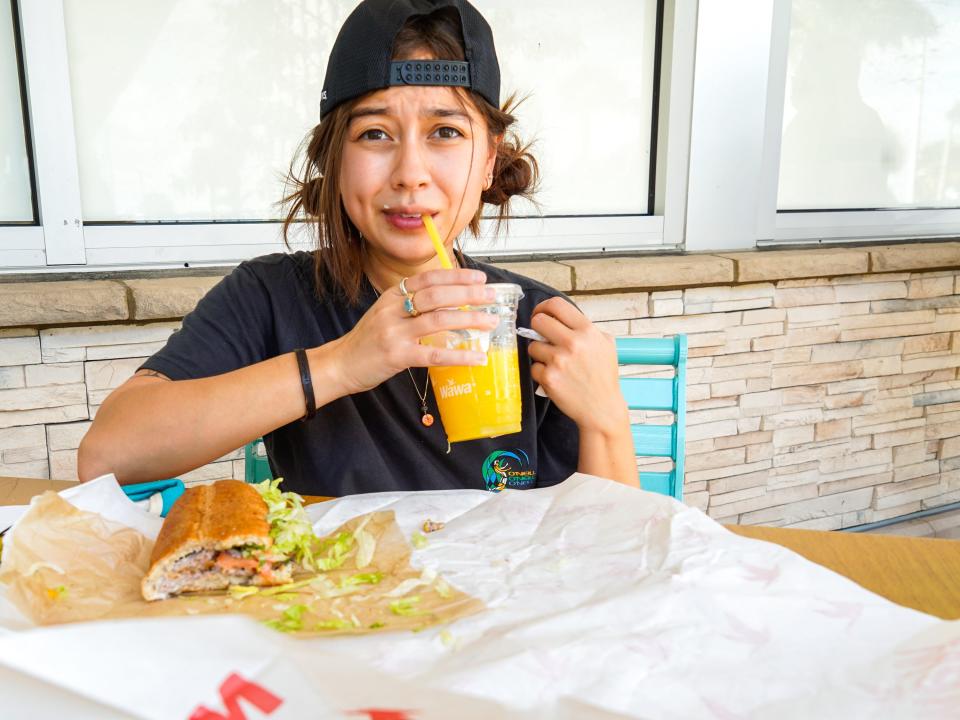 The author sips her orange juice outside of Wawa with her sandwich on he table in front of her