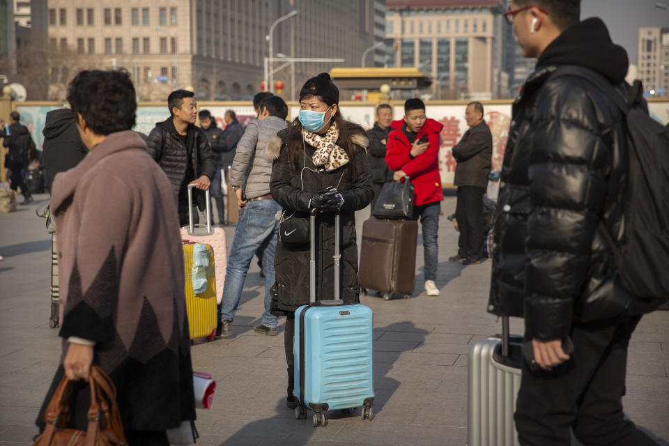 A traveler wears a facemask as she stands near the Beijing Railway Station in Beijing, Friday, Jan. 17, 2020. A second person has died from a new form of coronavirus in central China, health authorities said late Thursday. (AP Photo/Mark Schiefelbein)