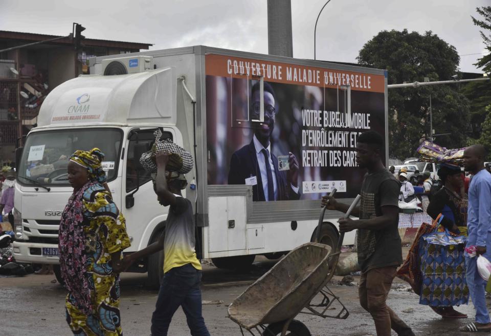 Residents walk past a mobile enrolment center from the Ivory Coast health authorities in Abidjan Monday, June 10, 2024. The country's universal health coverage program, has been criticized since its inception in 2019 for an inefficient voucher system that has made it impossible for participants to access the benefits. The mobile enrolment centers allow Ivorians to sign up for the scheme and provide them with cards on site, so that they can start receiving care immediately at hospitals, clinics, and pharmacies around the country. (AP Photo/ Diomande Ble Blonde)