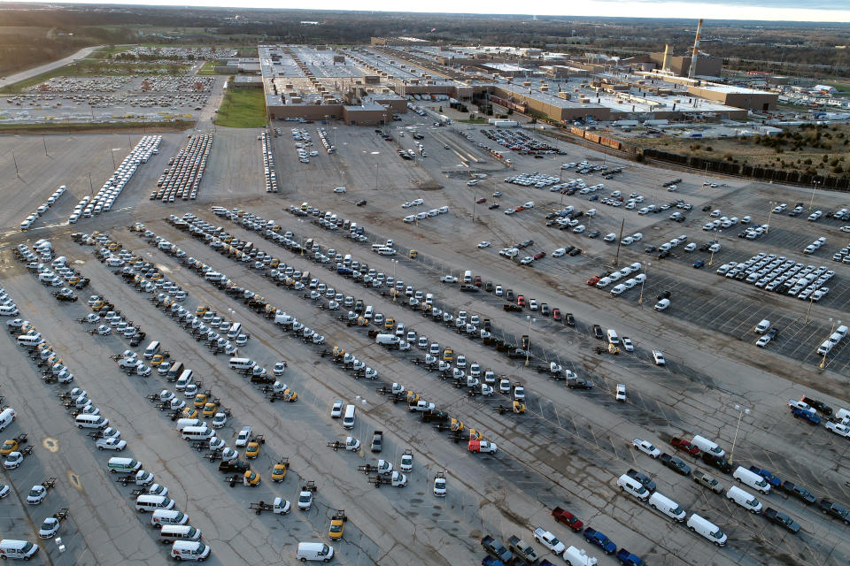 In this aerial photo, a General Motors assembly plant is seen at top right while mid-sized pickup trucks and full-size vans currently produced at the plant are seen in a parking lot outside Wednesday, March 24, 2021, in Wentzville, Mo. As the U.S. economy awakens from its pandemic-induced slumber, a vital cog is in short supply: the computer chips that power our cars and other vehicles, and a vast number of other items we take for granted. Ford, GM and Stellantis have started building vehicles without some computers, putting them in storage with plans to retrofit them later. (AP Photo/Jeff Roberson)