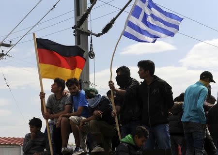 Migrants and refugees hold German and Greek flags as they sit on top of a train carriage at a makeshift camp at the Greek-Macedonian border near the village of Idomeni, Greece, April 11, 2016. REUTERS/Alexandros Avramidis