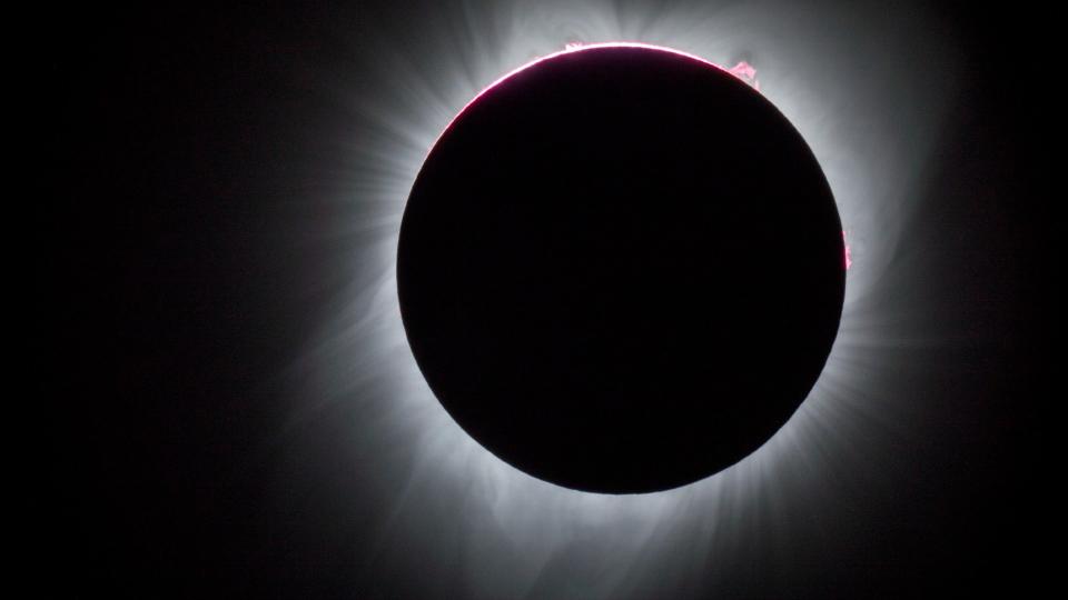 a total solar eclipse seen against a black sky shows the sun blocked by the moon with a white outflow behind which is the sun's outer atmosphere.