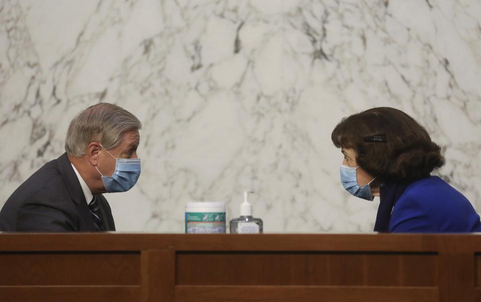 With wipes and hand sanitizer between them, Lindsey Graham and Dianne Feinstein, wearing masks, chat.