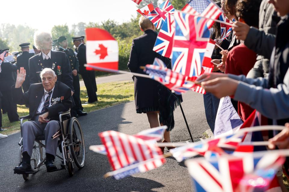 People wave flags for World War II veterans before a ceremony at the Pegasus Bridge memorial in Benouville, Normandy, Monday June 5, 2023.