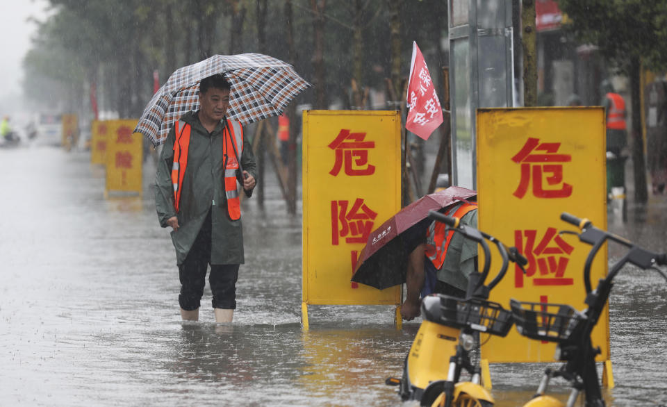 In this photo released by Xinhua News Agency, staff members set up warning signs with the words "Danger!" at a waterlogged area in Wuzhi County in central China's Henan Province on Tuesday, July 20, 2021. At least a dozen people died in severe flooding Tuesday in a Chinese provincial capital that trapped people in subways and schools, washed away vehicles and stranded people in their workplaces overnight. (Feng Xiaomin/Xinhua via AP)