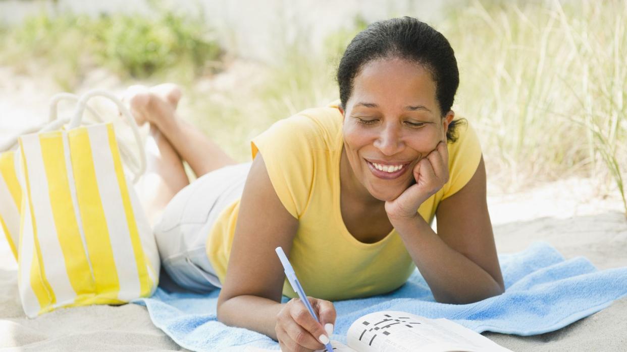 black woman doing crossword puzzle on beach