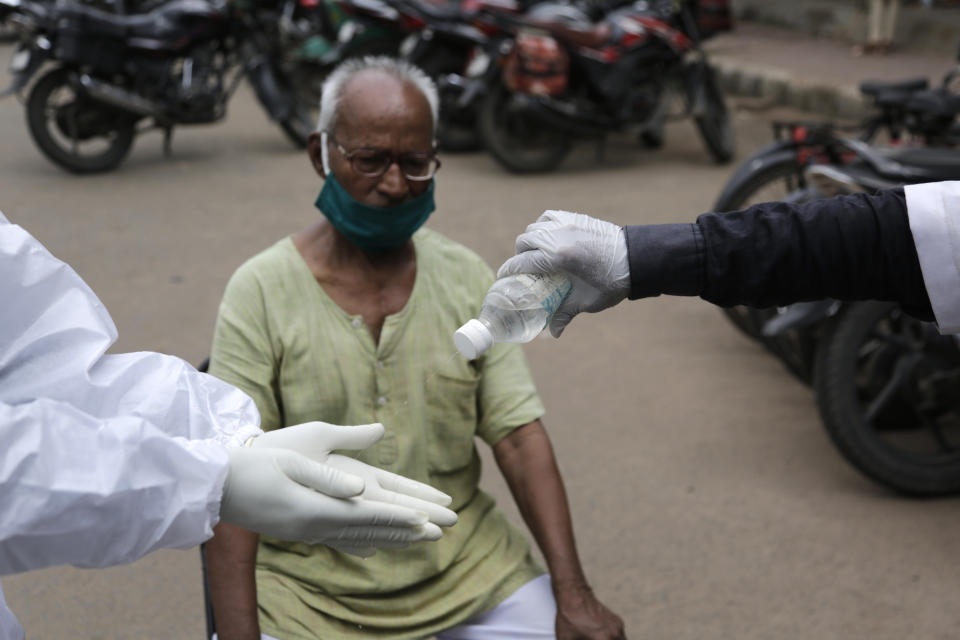 An Indian health worker sprays sanitizer to other's hands after taking a swab sample of a man for COVID-19 test in Ahmedabad, India, Friday, July 24, 2020. India is the third hardest-hit country by the pandemic in the world after the United States and Brazil. (AP Photo/Ajit Solanki)