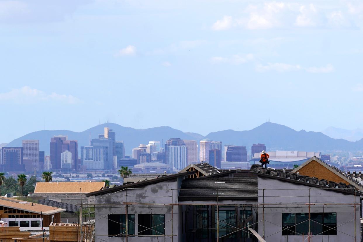 In this Aug. 12, 2021, file photo with the downtown skyline in the background, a roofer works on a new home being built in a new housing development as expansive urban sprawl continues in Phoenix.