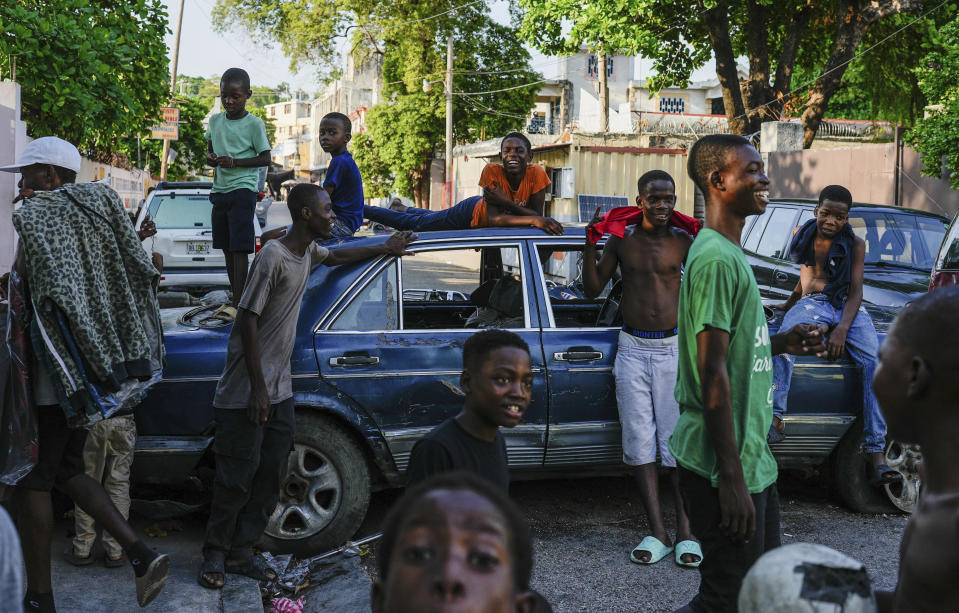 Varios jóvenes, junto a autos que sirven de barricadas instaladas por los residentes para frenar la entrada de las bandas en su vecindario, en el centro de Puerto Príncipe, Haití, el 17 de mayo de 2024. (AP Foto/Ramón Espinosa)