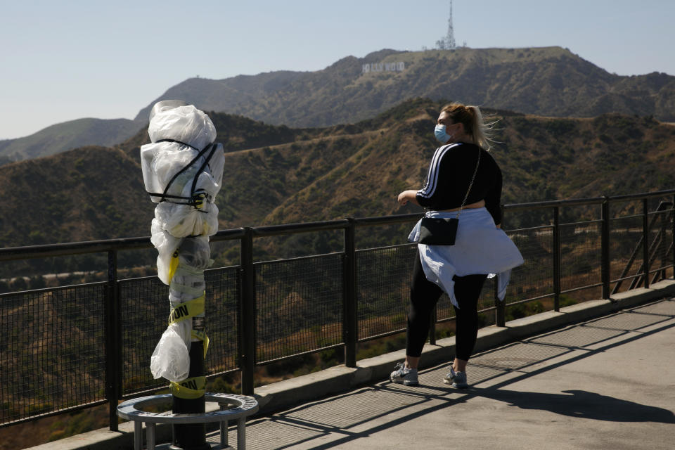 A woman with a face mask stands next to a telescope wrapped in plastic to prevent the spread of COVID-19 at the Griffith Observatory overlooking downtown Los Angeles, Wednesday, July 15, 2020. Coronavirus cases have surged to record levels in the Los Angeles area, putting the nation's largest county in "an alarming and dangerous phase" that if not reversed could overwhelm intensive care units and usher in more sweeping closures, health officials said Wednesday. (AP Photo/Jae C. Hong)