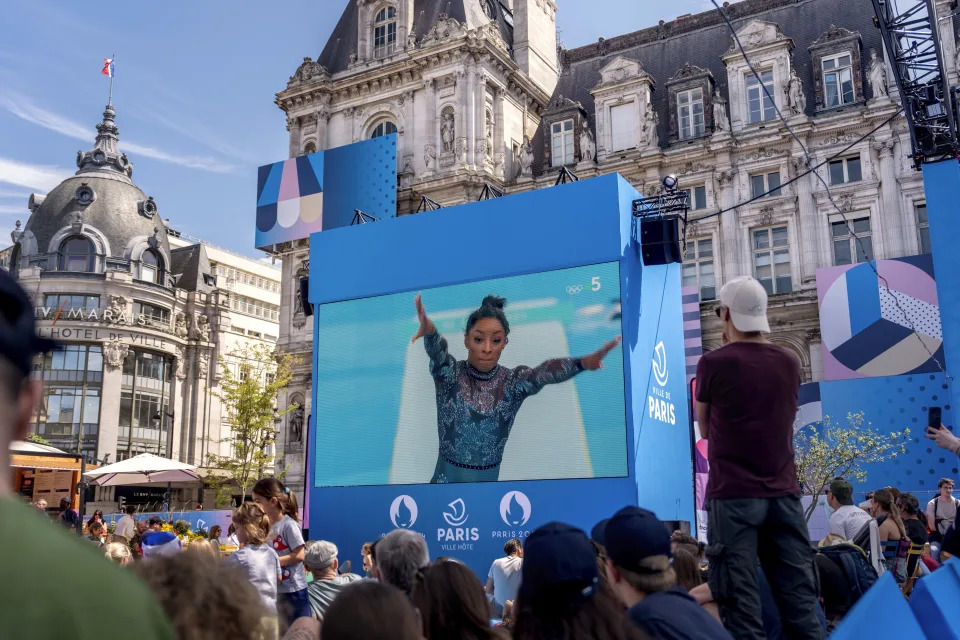 Spectators watch from a fan zone set up at the Hotel de Ville, the city hall, as Simone Biles, of the United States, performs on the vault during a women's artistic gymnastics qualification round at the 2024 Summer Olympics, Sunday, July 28, 2024, in Paris. (AP Photo/David Goldman)