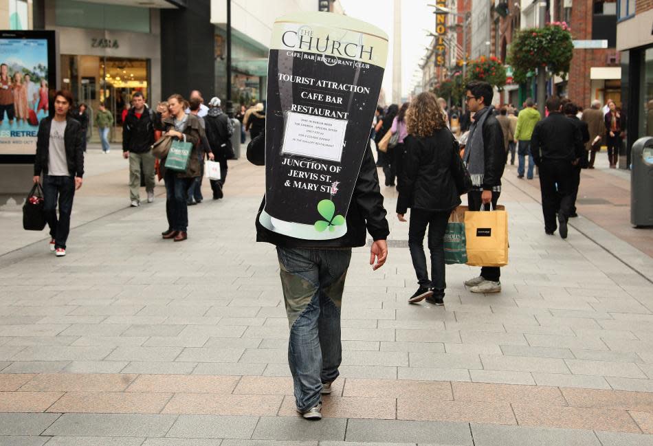 A man with an advertising hoarding on his back walks down the street in Dublin, Ireland.