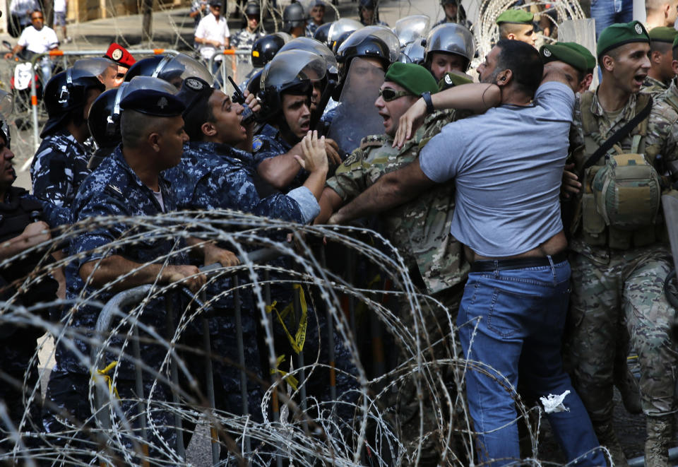 Lebanese army soldiers and riot policemen, left, stop a retired soldier, center right, who is trying to cross the barbed wires and enter to the parliament building where lawmakers and ministers are discussing the draft 2019 state budget, in Beirut, Lebanon, Friday, July 19, 2019. The budget is aimed at averting a financial crisis in heavily indebted Lebanon. But it was met with criticism for failing to address structural problems. Instead, the budget mostly cuts public spending and raises taxes. (AP Photo/Hussein Malla)