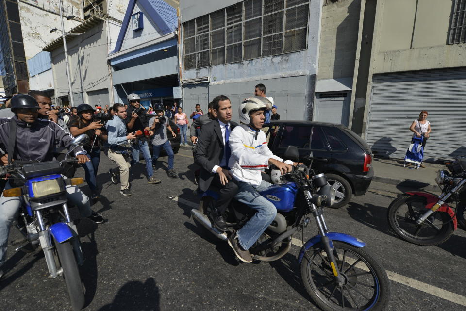 Opposition leader Juan Guaido rides on the back of a motorcycle, toward buses carrying opposition lawmakers that are blocked by security forces, as their group travels to attend a session at the National Assembly in Caracas, Venezuela, Tuesday, Jan. 7, 2020. Venezuela’s opposition is facing its biggest test yet after government-backed lawmakers announced they were taking control of what Guaidó supporters have described as the nation’s last democratic institution. (AP Photo/Matias Delacroix)