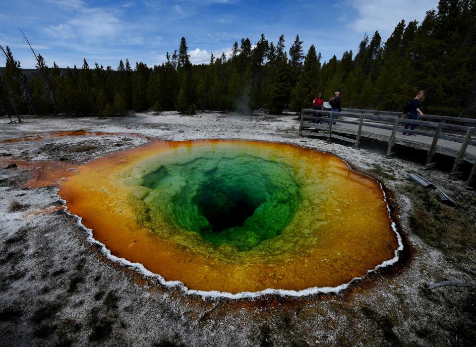 Tourists view the Morning Glory hot spring in the Upper Geyser Basin of Yellowstone National Park in Wyoming, on May 14, 2016. 
The distinctive colors of the hot spring is due to bacteria which survive in the hot water although its vivid color has changed from its original blue to yellow and green after an accumulation of coins and debris thrown by tourists.