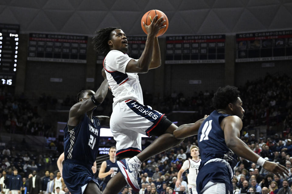 UConn guard Tristen Newton, center, jumps to the basket between New Hampshire forward Clarence Daniels (21) and guard Christian Moore (11) in the first half of an NCAA college basketball game, Monday, Nov. 27, 2023, in Storrs, Conn. (AP Photo/Jessica Hill)
