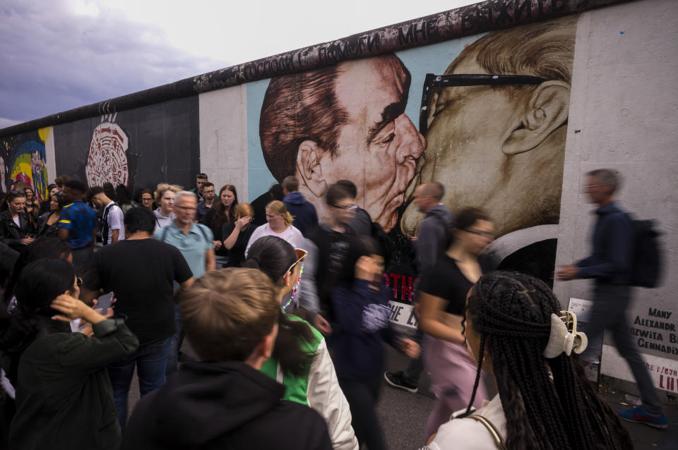 Tourists gather in front of the popular 'My God, Help Me to Survive This Deadly Love' painting by Dmitri Vrubel, at the East Side Gallery, of what remains of the Berlin Wall, in Berlin, Germany, Monday, July 3, 2023. Crowds are packing the Colosseum, the Louvre, the Acropolis and other major attractions as tourism exceeds 2019 records in some of Europe’s most popular destinations. While European tourists helped the industry on the road to recovery last year, the upswing this summer is led largely by Americans, who are lifted by a strong dollar and in some cases pandemic savings. (AP Photo/Markus Schreiber)