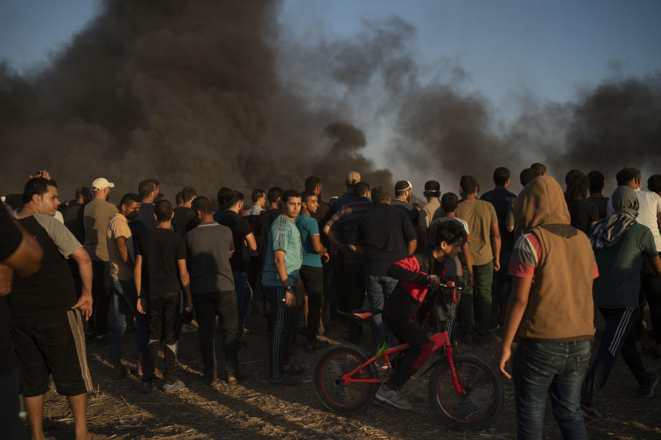 In this Friday, Sept. 14, 2018 photo, a boy rides his bike as Palestinians gather during a protest at the Gaza Strip's border with Israel, east of Gaza City. Eight months after demonstrations against Israel’s long blockade of Gaza began, the casualty toll keeps rising, and there is no end in sight. (AP Photo/Felipe Dana)