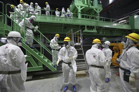 Members of the media and Tokyo Electric Power Co. (TEPCO) employees wearing protective suits and masks walk down the steps of a fuel handling machine on the spent fuel pool inside the No.4 reactor building at the tsunami-crippled TEPCO's Fukushima Daiichi nuclear power plant in Fukushima prefecture in this November 7, 2013 file photo. REUTERS/Tomohiro Ohsumi