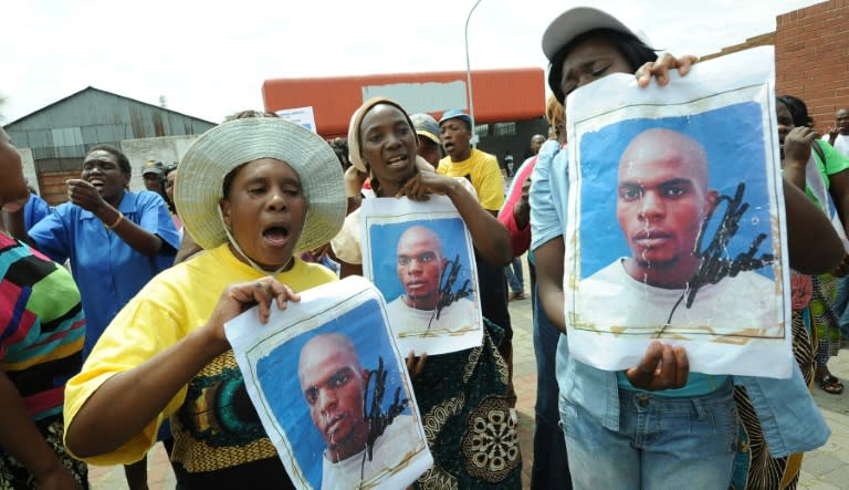 (FILES) -- This file photo taken on March 8, 2013 in Benoni shows protestors holding portraits of Mozambican taxi driver Mido Macia outside the Benoni court where police officers were charged with murdering him on February 26, 2013 in Daveyton, east of Johannesburg. Eight South African policeman were on August 25, 2015 found guilty of murdering a Mozambican man who died after being dragged behind a moving police van two years ago. The 27-year-old taxi driver died in police custody after being arrested for parking his car on the wrong side of the road. AFP PHOTO / ALEXANDER JOE