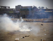 A tear gas shell explodes near policemen after it was thrown back by protesting farmers, at the border between Delhi and Haryana state, Friday, Nov. 27, 2020. Thousands of agitating farmers in India faced tear gas and baton charge from police on Friday after they resumed their march to the capital against new farming laws that they fear will give more power to corporations and reduce their earnings. While trying to march towards New Delhi, the farmers, using their tractors, cleared concrete blockades, walls of shipping containers and horizontally parked trucks after police had set them up as barricades and dug trenches on highways to block roads leading to the capital. (AP Photo/Manish Swarup)