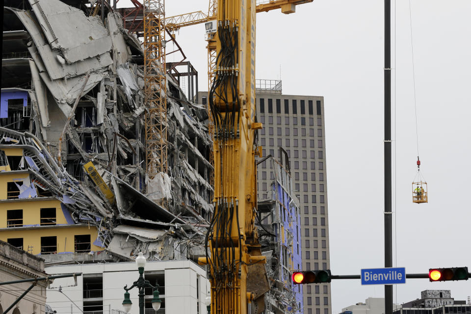 Workers in a bucket, right, begin the process of planting explosive charges on two unstable cranes at the Hard Rock Hotel, which underwent a partial, major collapse on Saturday, Oct. 12, in New Orleans, viewed on Thursday, Oct. 17, 2019. Authorities say explosives will be strategically placed on the two unstable construction cranes in hopes of bringing them down with a series of small controlled blasts ahead of approaching tropical weather. Officials hope to bring the towers down Friday without damaging nearby businesses and historic buildings in and around the nearby French Quarter. (AP Photo/Gerald Herbert)