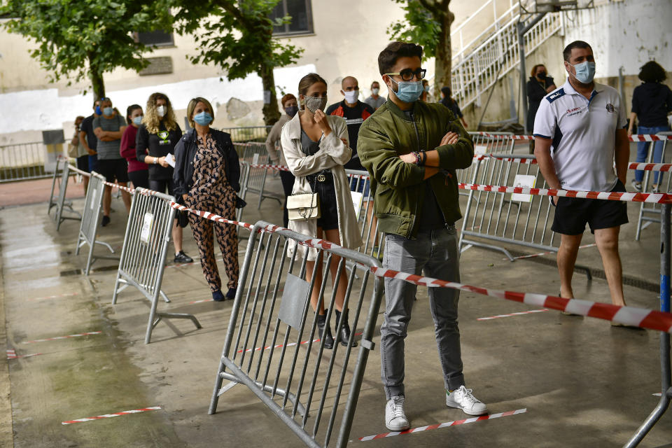 People wait in a queue outside of a polling station, while wearing face masks to help curb the spread of the coronavirus, during the Basque regional election in the village of Ordizia, northern Spain, Sunday, July 12, 2020. Basque authorities are displaying special rules and practices in the protection against the coronavirus. (AP Photo/Alvaro Barrientos)