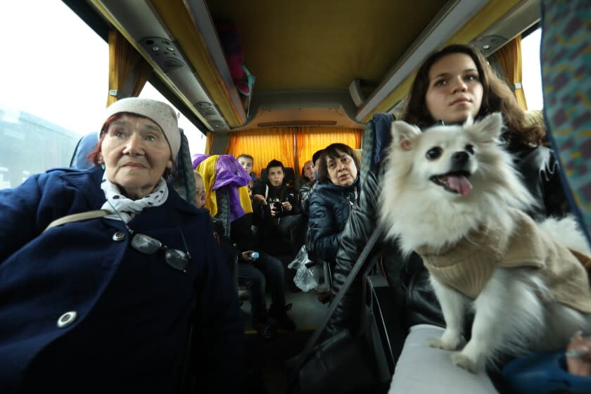 ISACCEA, ROMANIA-APRIL 10, 2022-Nataliia (double ii) Cherneha age 78, left, Melek Sidorova, right, with her dog Lea, and other Ukrainians board a bus at the Isaccea, Romania border crossing before heading to Bucharest. She left Mykolaiv with her daughter and grandchildren. Despite a day and night curfew in southern Ukraine, which restricted travel, dozens of refugees made it to the Orlivka Ferry crossing which goes across the Danube to Isaccea, Romania. (Carolyn Cole / Los Angeles Times)