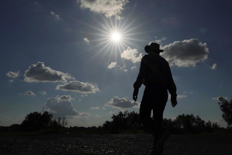 FILE - Kayak and canoe outfitter Jessie Fuentes walks along the Rio Grande under a warm sun Thursday, July 6, 2023. As the heat breaks records, weakening and sickening people, it’s worth remembering that dire heat waves have inspired effective efforts to prevent heat illness. (AP Photo/Eric Gay, File)