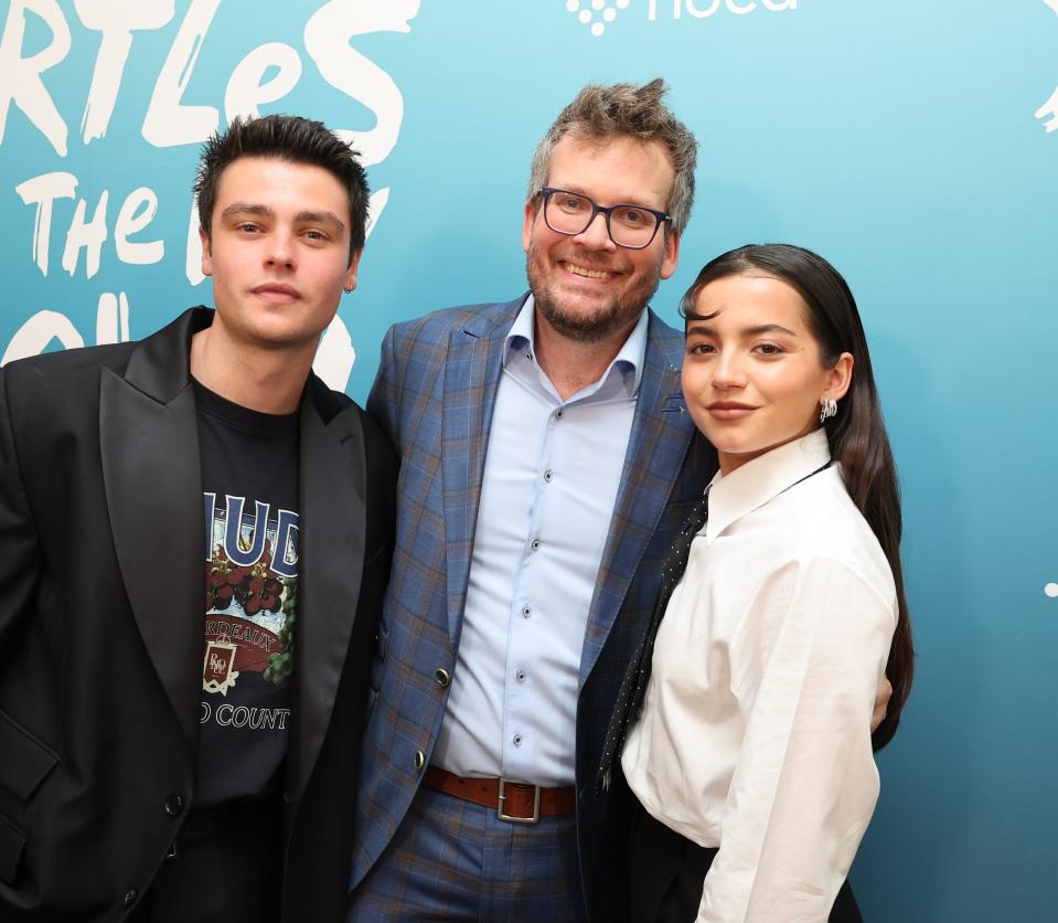 Three people posing at an event, flanked by a backdrop with text and a turtle graphic