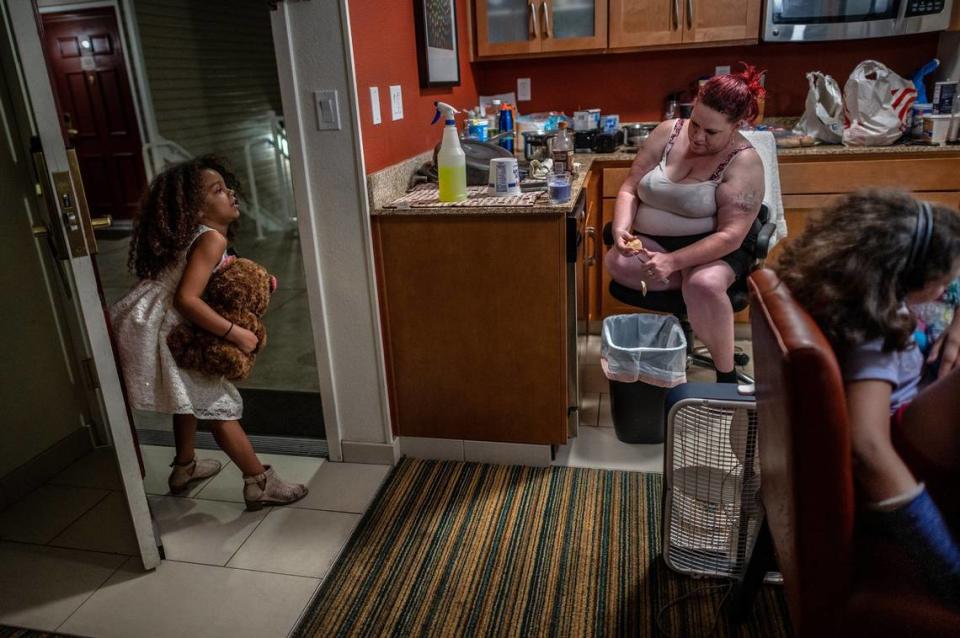 Kristi Phillips peels a potato inside a room at a Sacramento Residence Inn as her daughter Shyann heads outside with her teddy bear to join her father in May 2021.