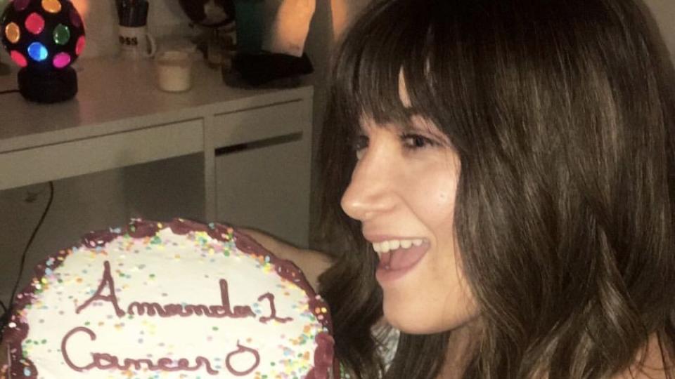 the author in a wig holding a cake that reads amanda 1 cancer 0