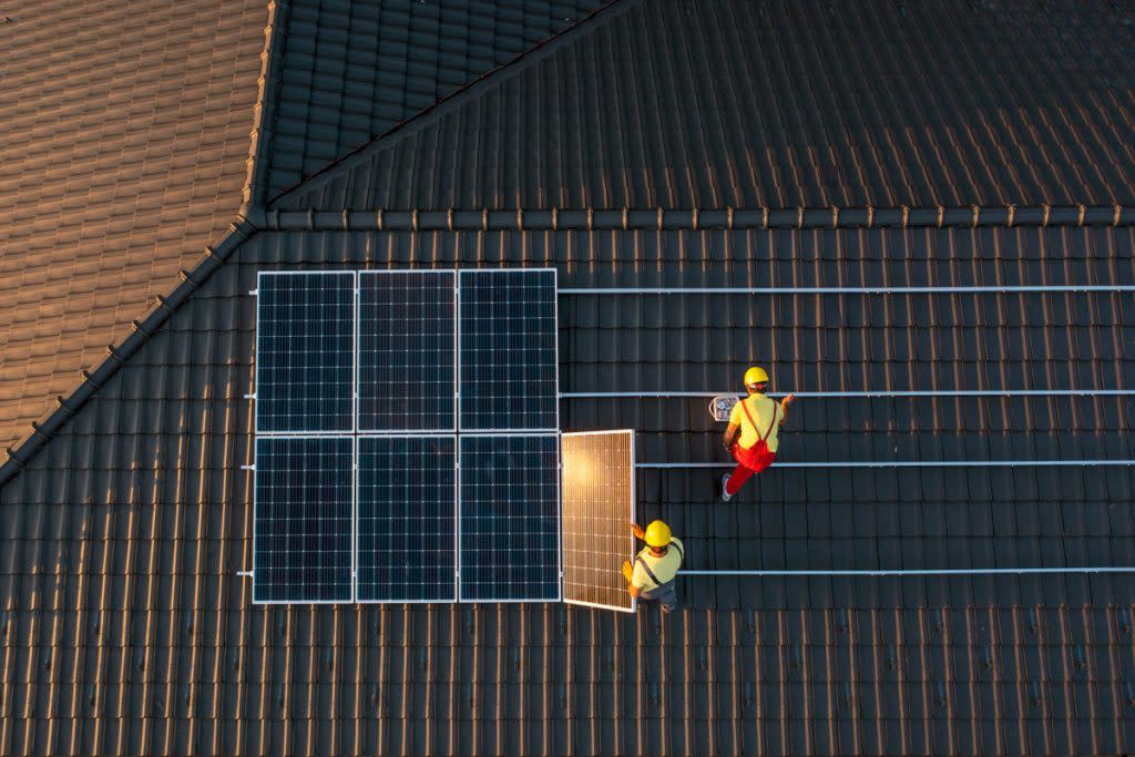 Two men put solar panels on a person's roof. 