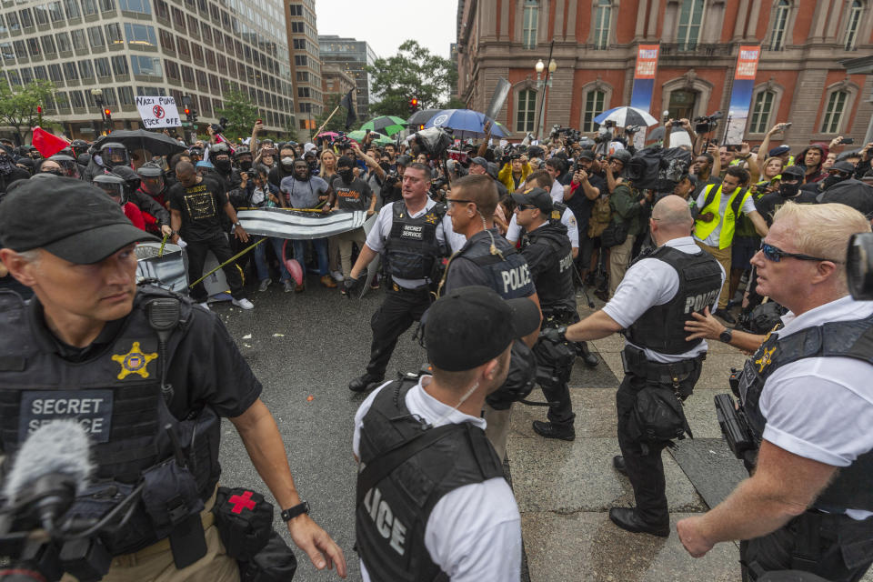 Metro Police and Secret Service personnel are forced back by counter-protesters outside of the Pennsylvania Avenue security barrier on 17th street while attempting to escort attendees of the "Unite the Right 2" rally from Lafayette Park in Washington, Sunday, Aug. 12, 2018. (Craig Hudson/Charleston Gazette-Mail via AP)