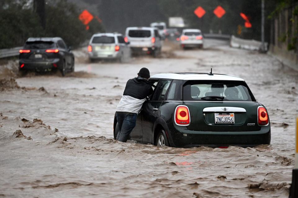 A man pushes a stalled car on a flooded highway
