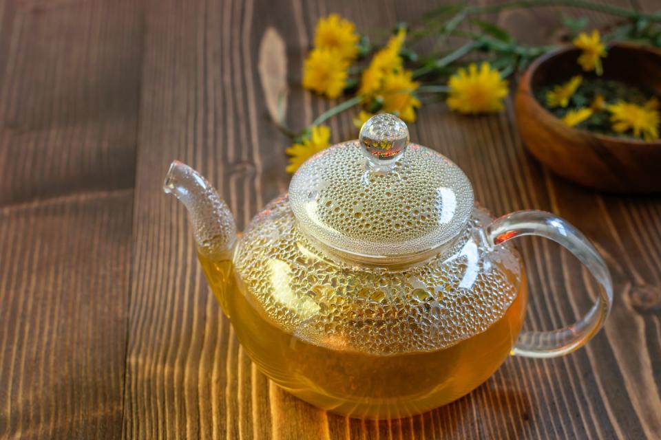 glass teapot with golden dandelion tea on the wooden table