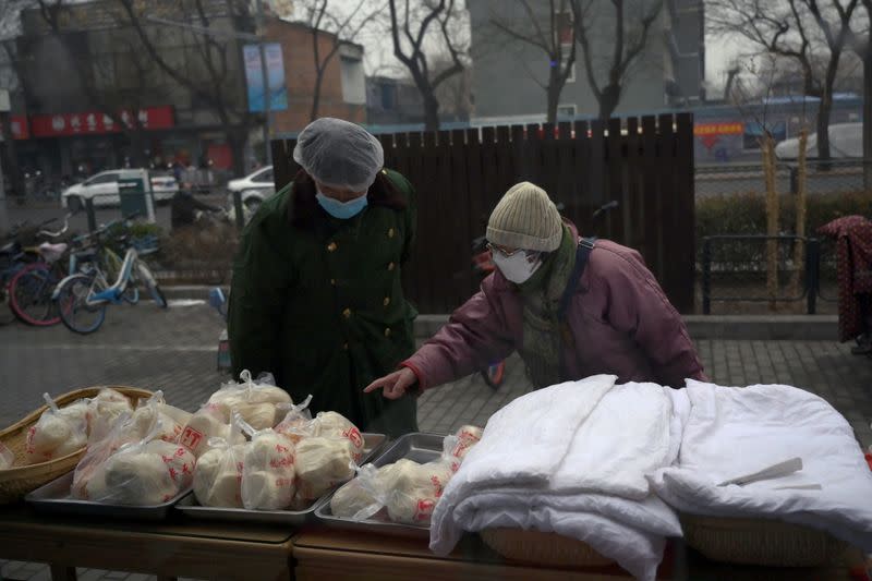 Woman wearing a face mask buys food from a stall set up by a restaurant outside its outlet in Beijing