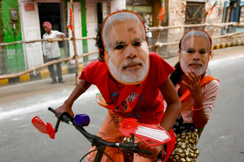 Children riding a bicycle wear masks portraying Narendra Modi in Varanasi (AFP)