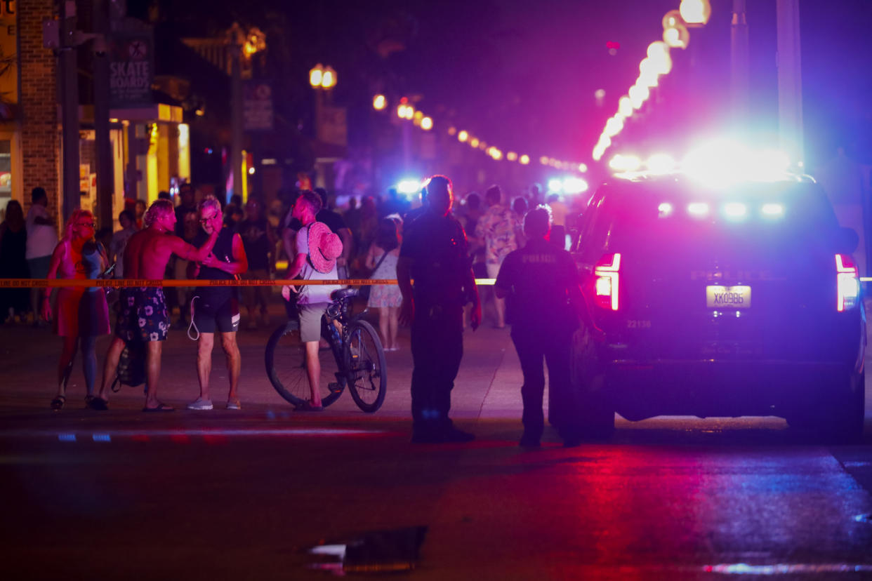 Two law enforcement officers stand near their vehicle on a busy street at night.