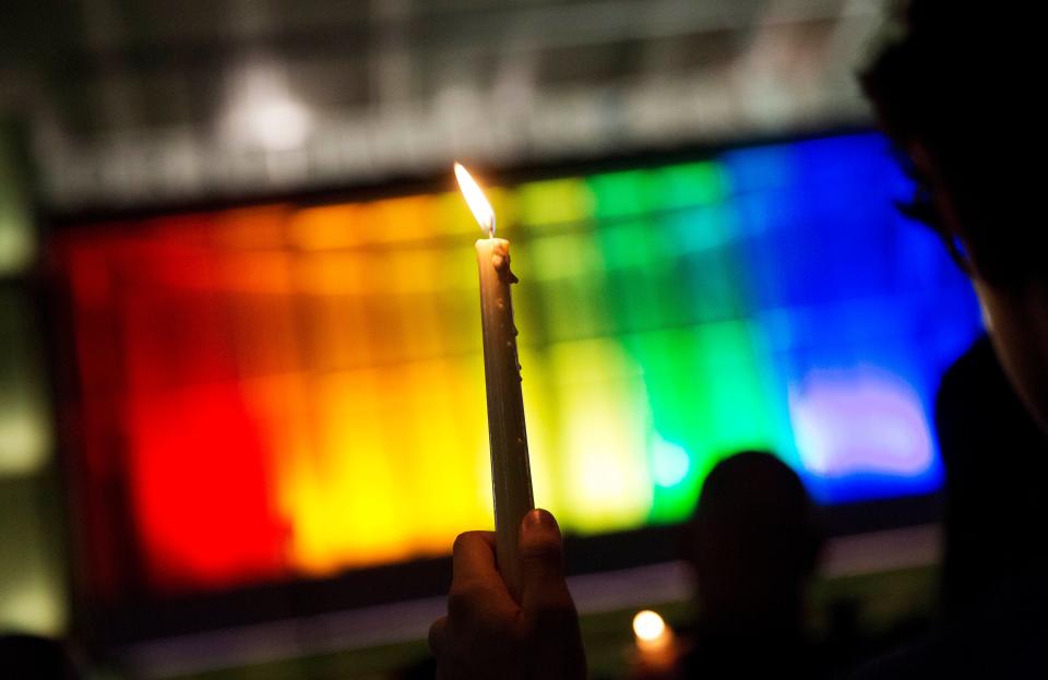 A mourner holds up candle against a rainbow lit backdrop during a vigil for those killed in a mass shooting at the Pulse nightclub downtown Monday, June 13, 2016, in Orlando, Florida.