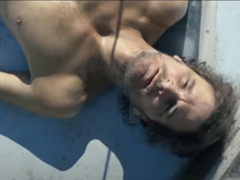 Colin Firth lying shirtless and disheveled on a boat.