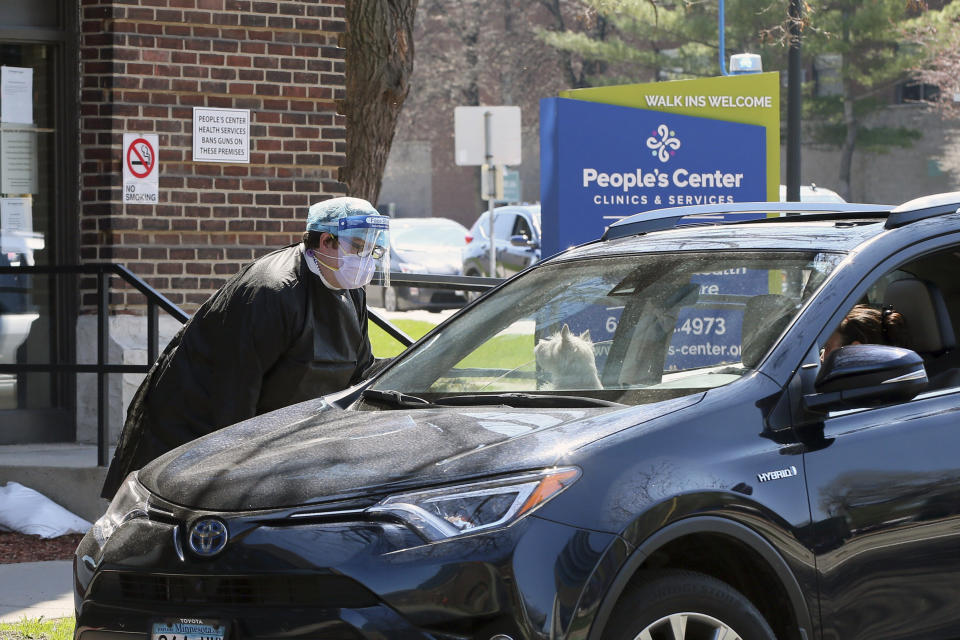 A dog checks out a health worker who talks to a driver in line for a coronavirus test at People's Center Monday, April 27, 2020, in Minneapolis during expanded coronavirus testing as Minnesota Gov. Tim Walz tries to get the numbers of tests up. Vice President Mike Pence is heading to Minnesota’s Mayo Clinic on Tuesday to learn about a new coronavirus testing “moonshot” that has the famed clinic joining with the state and the University of Minnesota to quickly boost the state's capacity to 20,000 tests a day. (AP Photo/Jim Mone)