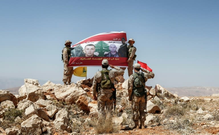 Hezbollah fighters giving a guided tour near the Lebanese-Syrian border on July 26, 2017 raise a Lebanese flag showing pictures of soldiers killed fighting jihadists